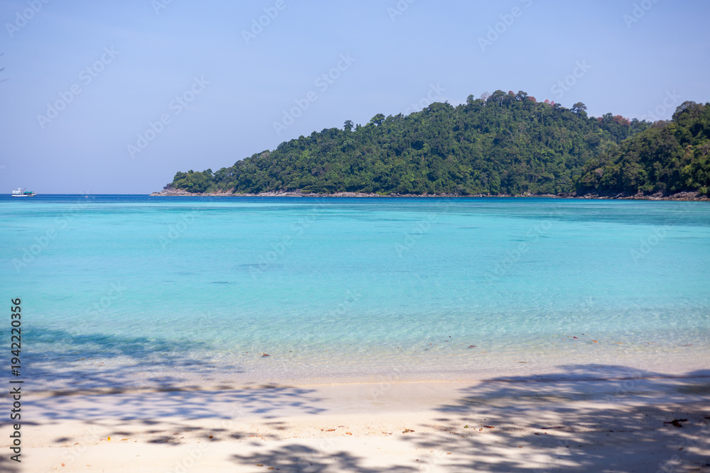 Obraz premium Tropical beach at Koh Surin, Ao Mai Ngam. Turquoise waters near sandy shoreline. Lush green island in background. Clear blue sky above sea.