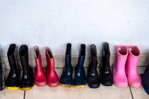Row of small children's pink and black rubber rain boots lined up in a Brazilian preschool hallway. Organized waterproof footwear ready for kids' outdoor play on a rainy school day