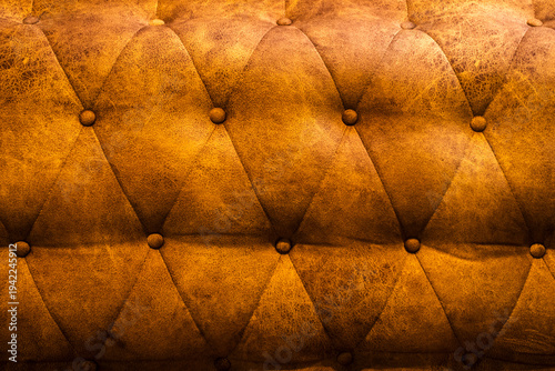 Close-up of a vintage brown tufted leather upholstery texture with a classic diamond pattern and decorative buttons, showing aged distressed material for luxury furniture background