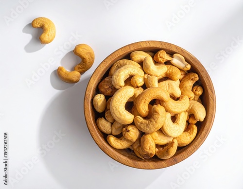 Top view of Roasted cashew nuts in wooden bowl with pile of cashew nuts on white background.