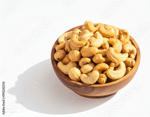 Top view of Roasted cashew nuts in wooden bowl with pile of cashew nuts on white background.