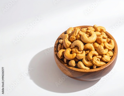Top view of Roasted cashew nuts in wooden bowl with pile of cashew nuts on white background.