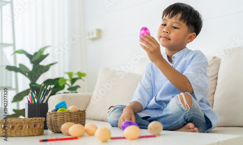 Cute asian little boy holding and looking at pink Easter egg at table in living room, Happy child playing with spring holiday decoration, Childhood development and fun celebration concept, Easter day