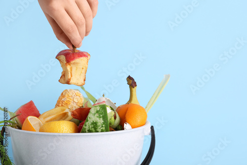 Foto Female hand putting apple core into bucket with organic waste on blue background