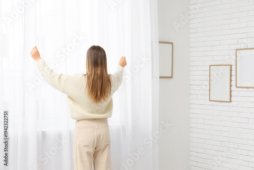 Photos Woman closing curtains in light room at home, back view