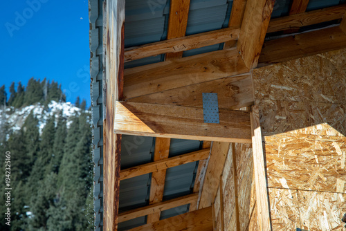 фотографія Close-up of a roof overhang construction showing wooden rafters, OSB sheathing, and metal roofing sheets under a clear blue sky