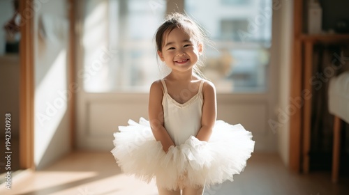 Happy little girl wearing a white ballet tutu dress smiling in a sunlit room.