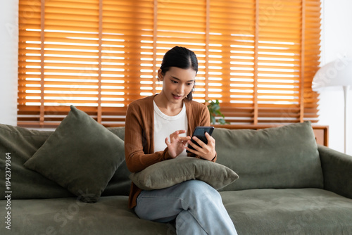 Happy young asian woman relax on comfortable couch at home texting messaging on smartphone, smiling girl use cellphone, chatting online message, shopping online from home
