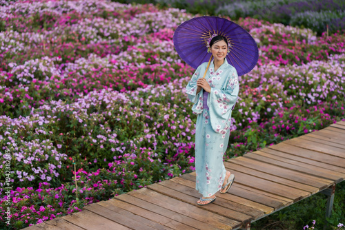 Fotografie woman in yukata (kimono dress) holding umbrella with flower blooming in garden