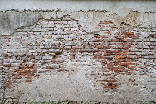 Photos Weathered surface of a historic brick wall features crumbling grey plaster that
