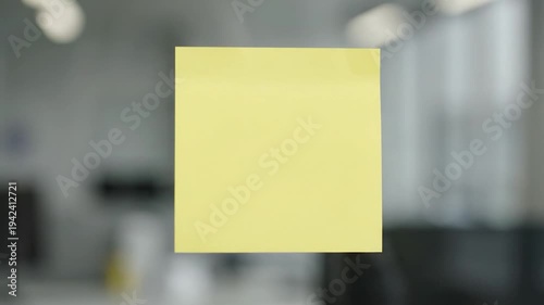 Yellow Sticky Note Attached to Glass Surface in Office Environment.