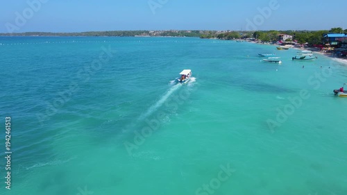 A small boat moves through the clear blue waters of Baru, revealing a vibrant beachside with colorful buildings.