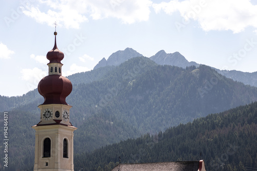 Fotografía The iconic red onion-domed bell tower of a traditional church stands prominently against the backdrop of the lush green slopes and rocky peaks of the Italian Dolomites in summer