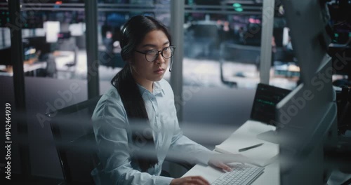 Asian Female Financial Specialist Sits at Innovative Workspace, Eyes Scanning Multiple Displays Filled With Trading Indices. Young Lady Actively Uses Keyboard to Input Data and Execute Market Orders.