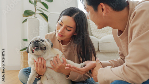 Asian couple playing with pug dog together at home