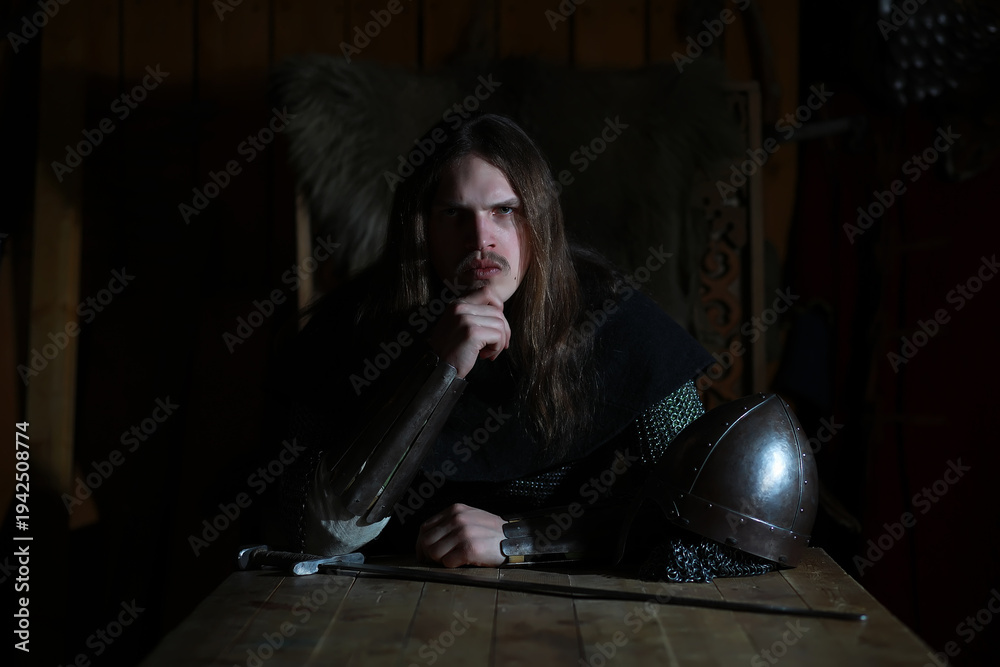 Fototapeta premium A mighty hero with long hair in chain mail armor in an ancient hall. Medieval warrior in the knight's chambers.