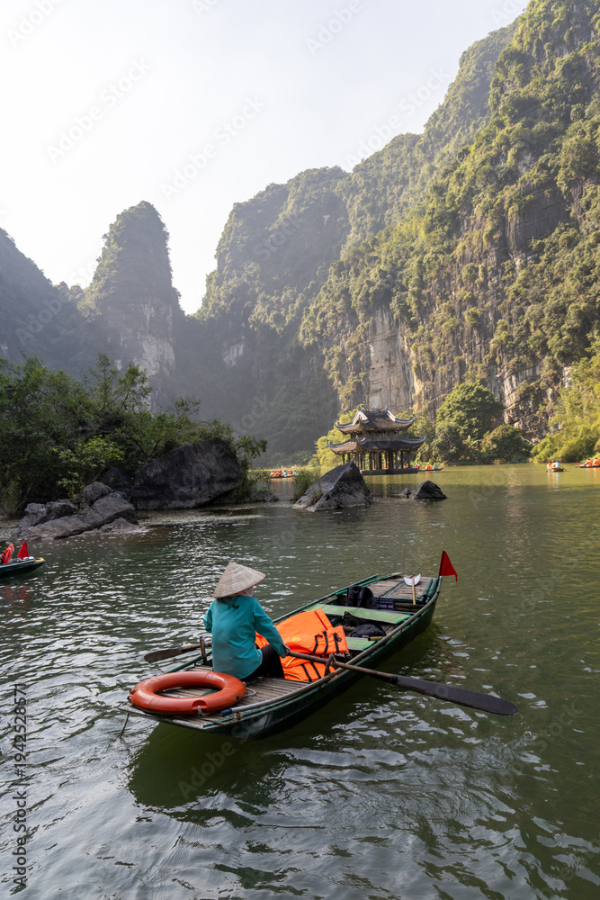 Fototapeta premium Tourists enjoy a boat tour of the Trang An river in Ninh Binh, Vietnam. The boats are rowed by local women, who take visitors to see the caves and limestone karsts.