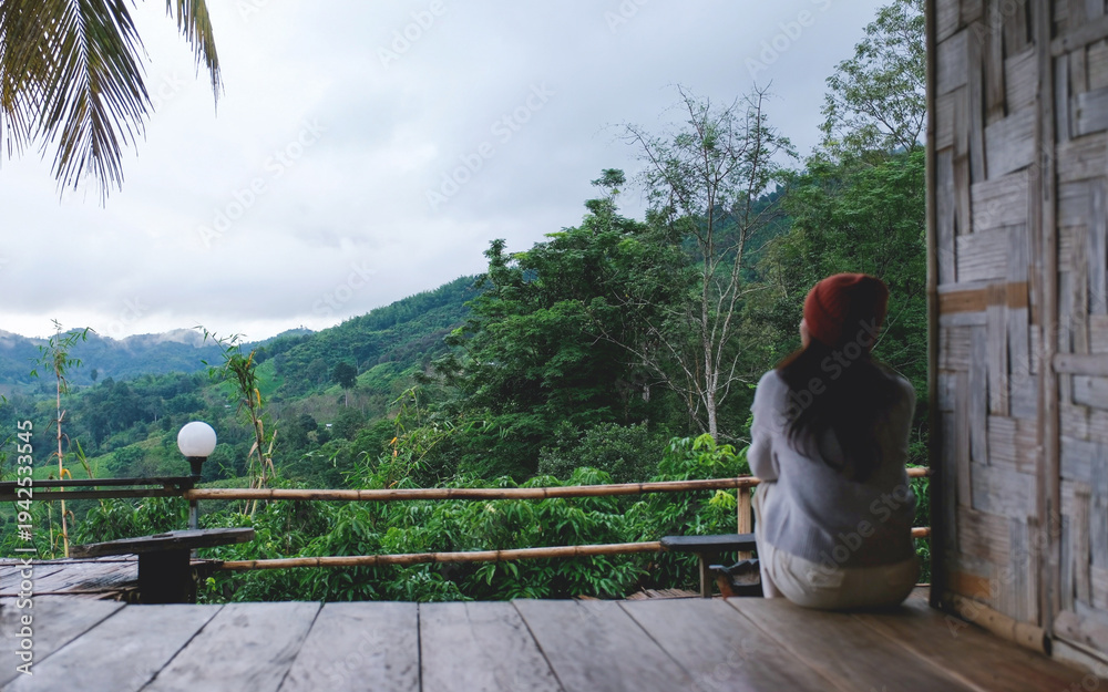 Naklejka premium Blurred of a woman sitting on wooden balcony, looking at mountain views on cloudy morning