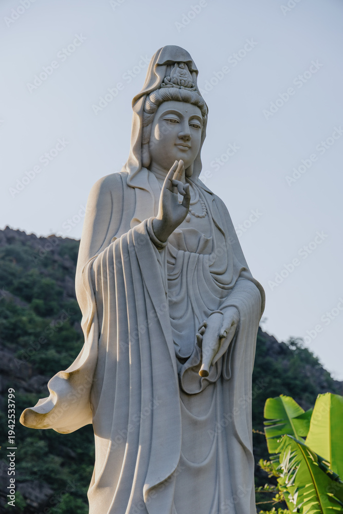 Fototapeta premium A serene Quan Am statue stands in Hoa Lu Ancient Capital, Ninh Binh, Vietnam. The statue is a symbol of compassion and mercy, inviting contemplation and peace.