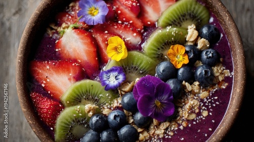 Colorful fruit bowl strawberries kiwi blueberries and flowers on wooden surface