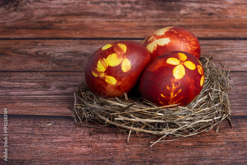 Easter eggs colored with onion peel in brown color, with flower pattern in straw nest on brown table background, Easter holiday table decoration, copy space    