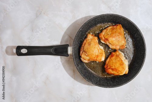 Foto Cooking chicken thighs in a frying pan on a marble countertop in a kitchen setti