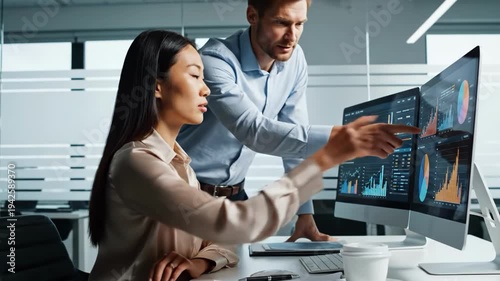 Two business professionals analyzing data on dual monitors in modern office