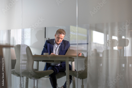 Senior businessman working while sitting at desk in office meeting room