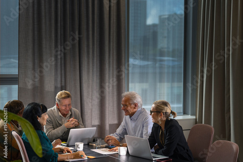 Group of smiling senior business professionals discussing while sitting around table in meeting room