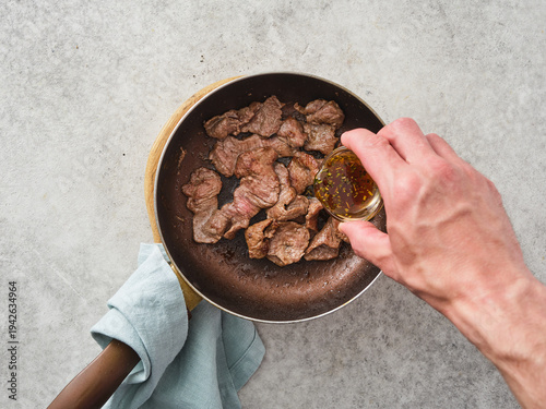 Quadro em tela Cooking beef pieces in a skillet with sauce preparation on a gray kitchen counte