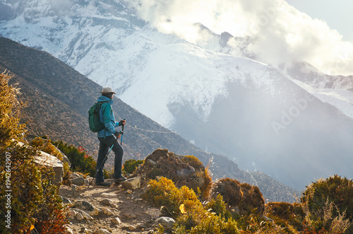 Woman hiker admires sunset on trail leading to Everest Base Camp with Himalayan Mountains surrounded by snow-capped peaks in background, Nepal.