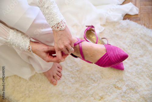 A bride's hands putting on her wedding shoes on her wedding day