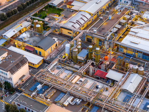 Aerial view of an industrial plant, with interconnected pipes and tanks casting long shadows under the warm light of dusk, Settecamini, Lazio, Italy.