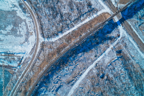 Rusty railway tracks and industrial train bridge crossing snowy winter rural landscape, desolate transport infrastructure, high angle drone shot