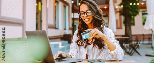 Tableau sur toile Portrait of woman holding bank card while sitting on cozy terrace in cafe
