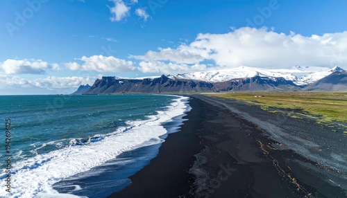 Aerial shot of black sand beach with ocean, mountains, and blue sky