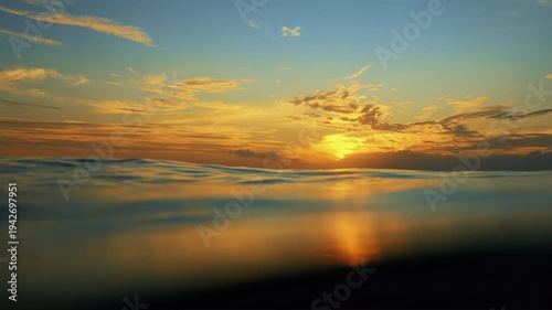 Slow Motion ocean surface from underwater at sunset with rays of light. Crystal clear breaking ocean wave with waving waterline. Sunrise over calm sea. Dawn over horizon, ocean, water - timelapse