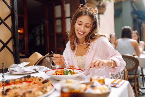 Bilde på lerret A happy woman eats fresh Italian pasta at a cafe table