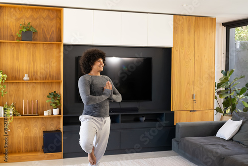 Man balancing in yoga pose in living room in sportswear near flat-screen TV with built-in shelving