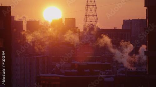 Golden sun rising over a frosty urban cityscape on a cold winter morning, with steam and smoke billowing from building chimneys against a clear sky, highlighting industrial activity