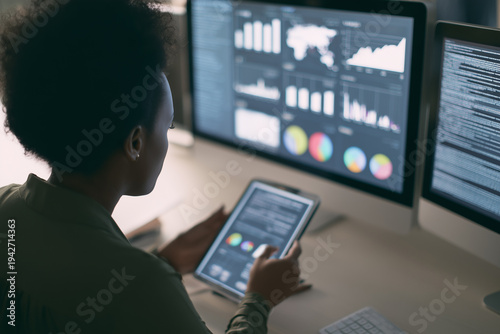 Woman sitting at multiple monitors working late night in office, analyzing stock charts and trading financial markets