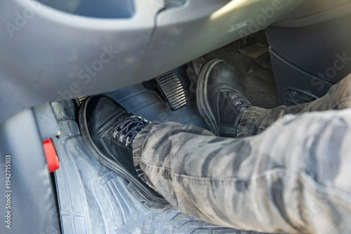Close up of driver feet in black leather boots pressing pedals in manual transmission car