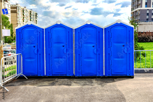 A row of blue portable toilet units is located outdoors.