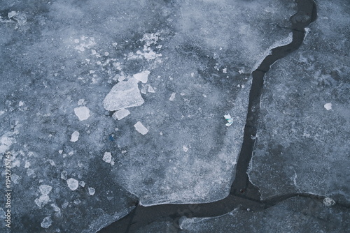 Close up view of a frozen surface featuring icy cracks and broken pieces of ice, reflecting a cold winter day.