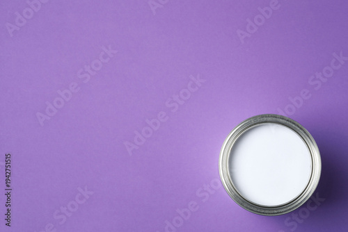 Can of bright paint and brush on purple background, top view
