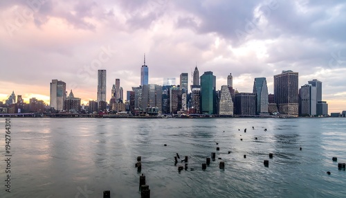 A scenic panoramic view of a large city skyline, its numerous skyscrapers reflecting in the water during an overcast sky