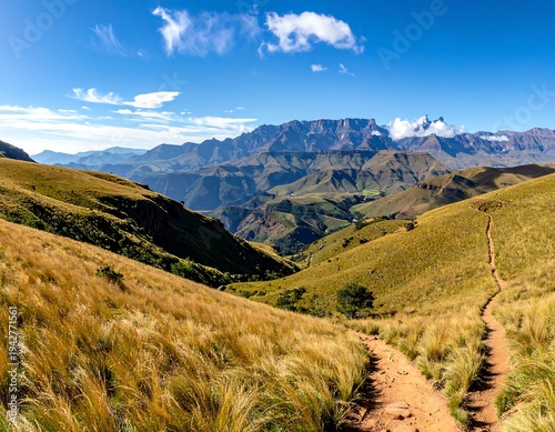 A scenic panoramic view of rolling hills and mountains under a bright blue sky with wispy clouds, featuring a winding path