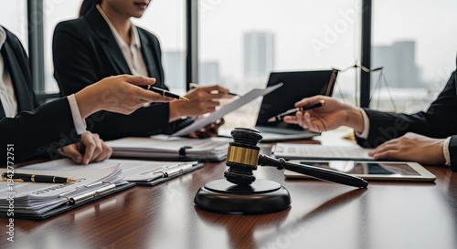 Several lawyers are gathered around a wooden table, reviewing legal documents. They are discussing a case, pointing at a document and a gavel.