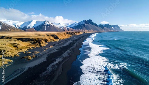 Aerial view of a black sand beach, mountains, and ocean under a blue sky