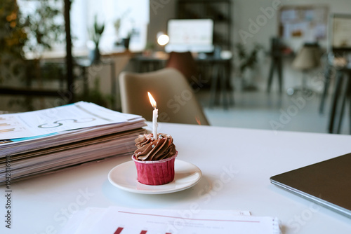 Картината върху платно Chocolate cupcake with single lit birthday candle standing on plate on office de